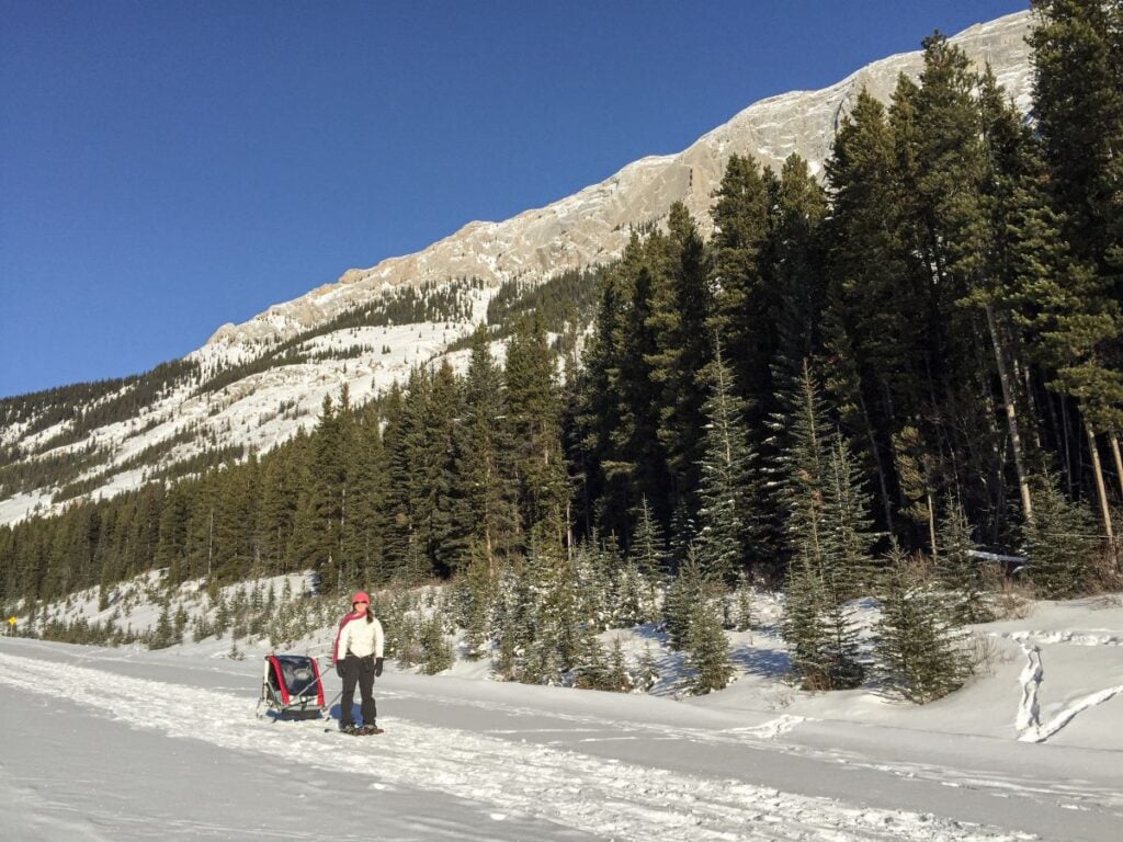 Celine Brewer, host of the Banff Travel Podcast, snowshoeing on Wintour Trail in Kananaskis Country while pulling her child in a Chariot.