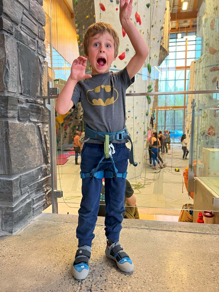 Things to do in Canmore with kids - Elevation Place Climbing Wall a boy hams it up outside the climbing wall at Elevation Place in Canmore, Alberta.