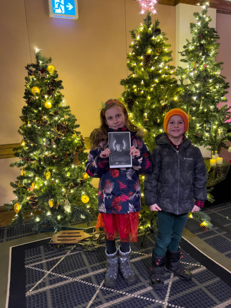 Brewer kids holding an “A Christmas Carol” program beside Christmas trees at the Banff Springs Hotel.