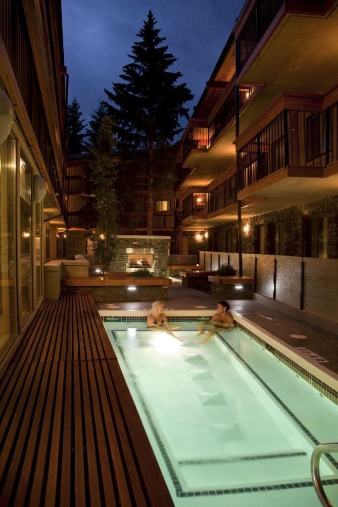 a luxurious, large outdoor hot tub is lit up at night at the Banff Aspen Lodge in downtown Banff.