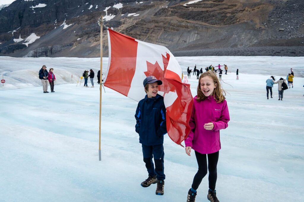 two kids on Athabasca Glacier next to a Canada Flag