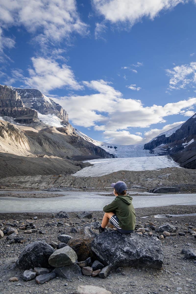 Toe ofthe Athabasca Glacier a boy sits looking at Athabasca Glacier from the Toe of the Athabasca Glacier trail