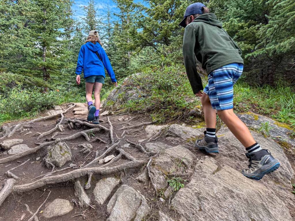 Two kids hike up a steep trail to the red chairs on Wilcox Pass in Jasper.