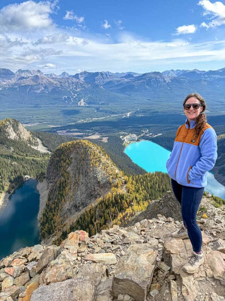 Celine Brewer, from the Travel Banff Canada blog, stands at the summit of the Devil's Thumb hike overlooking Lake Agnes and Lake Louise.
