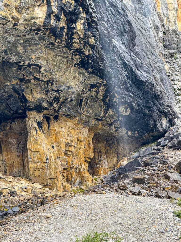 A wispy waterfall flows over black rocks on the Stanley Glacier hiking trail.