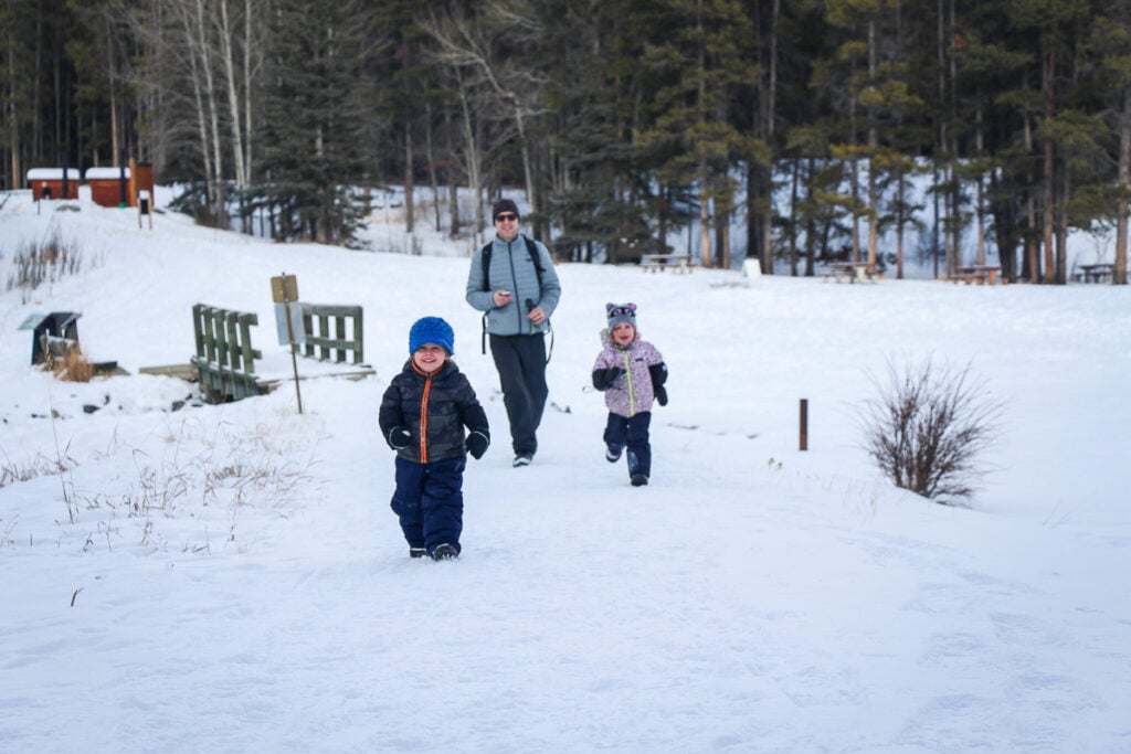 Dan Brewer, owner of TravelBanffCanada.com, walking with his kids on a snowy trail at Johnson Lake.