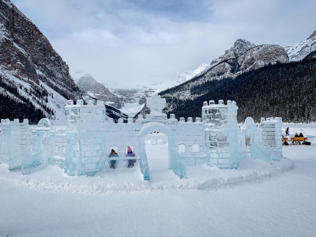 Two Brewer kids peek through the windows of an ice castle at Lake Louise in winter.
