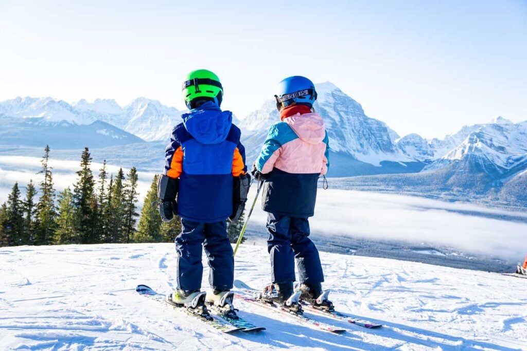 Two Brewer kids on skis looking out over snowy mountains at Lake Louise Ski Resort.