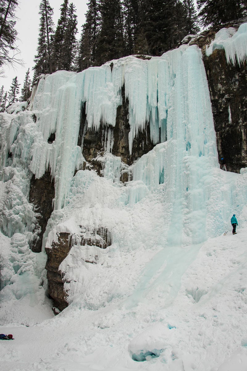 Towering frozen waterfall and a visitor beneath the icy cliffs at Johnston Canyon in winter.